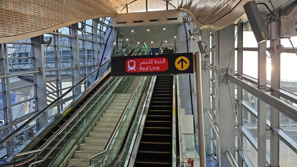 Interior view of a modern metro station with escalators leading to the Red Line, featuring a sign in Arabic and English.