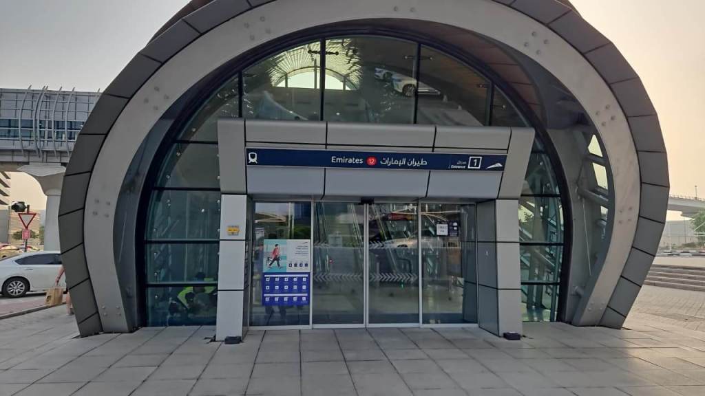 Entrance of Emirates Metro Station with a modern curved design and large glass doors, displaying signage in Arabic and English.