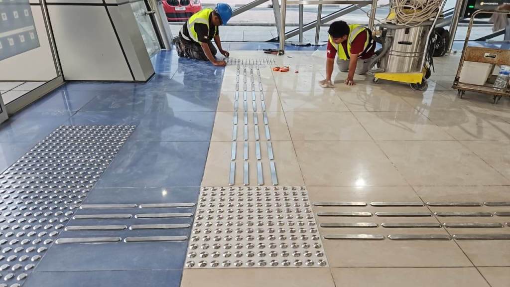 Two workers installing tactile paving and floor tiles in a commercial space.