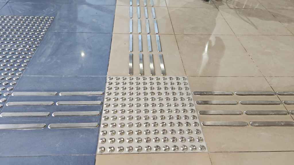 A close-up view of textured flooring with different tactile patterns, including smooth strips and raised dots, designed for accessibility.