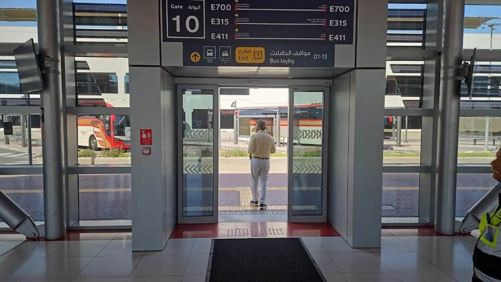 Interior view of an airport terminal showing Gate 10, with a passenger walking towards the exit and buses visible outside.