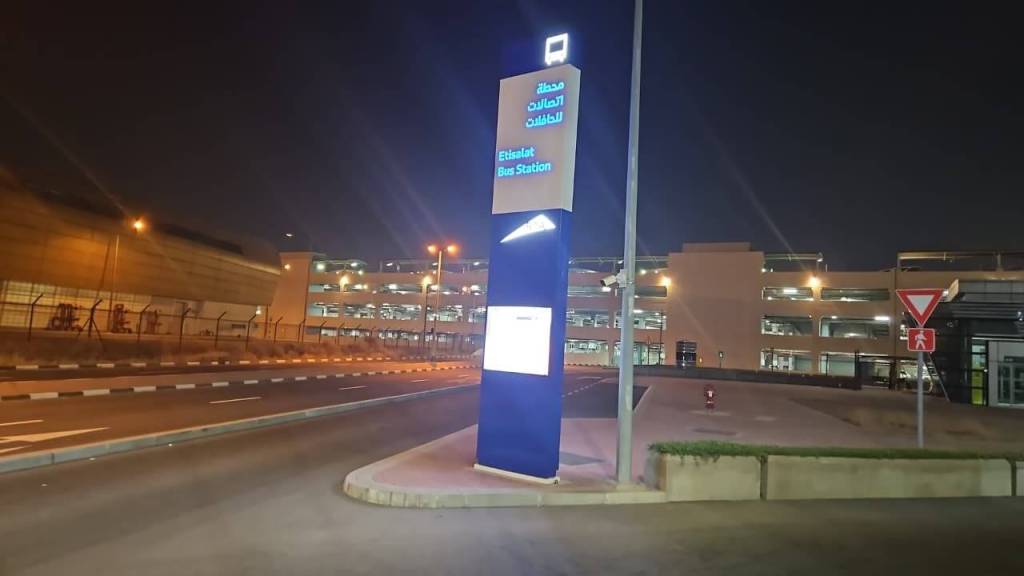 Illuminated sign for Etisalat Bus Station at night, showing both Arabic and English text.