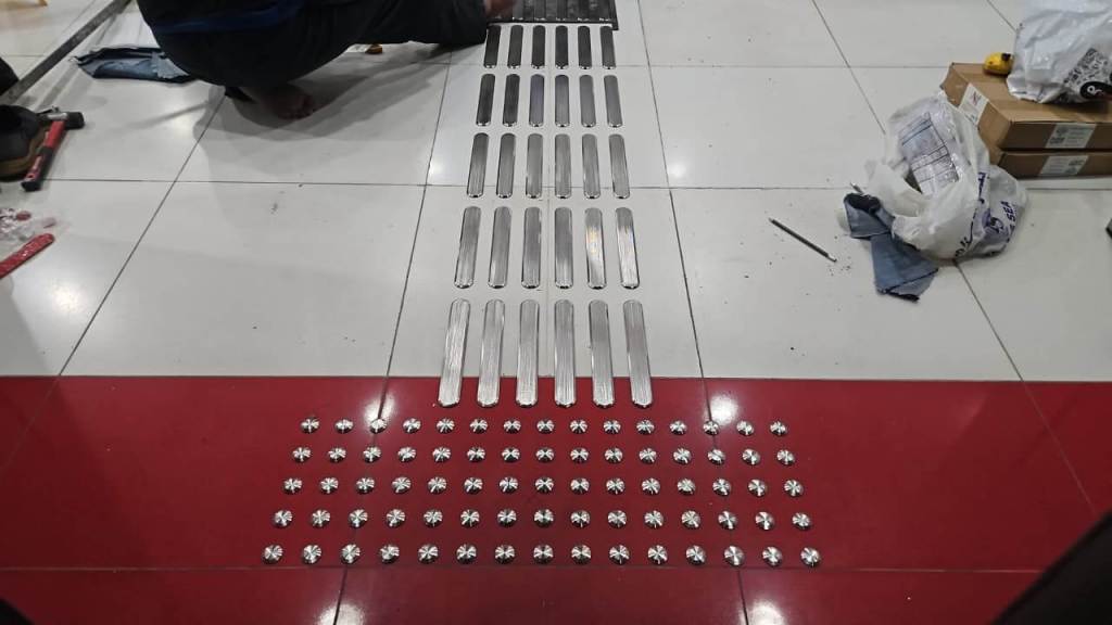 A person installing metal strips and small circular fixtures on a tiled floor, focusing on accessibility improvements.