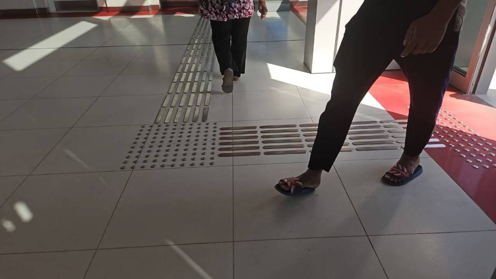 Two people walking on a tiled floor with tactile paving indicators for the visually impaired.