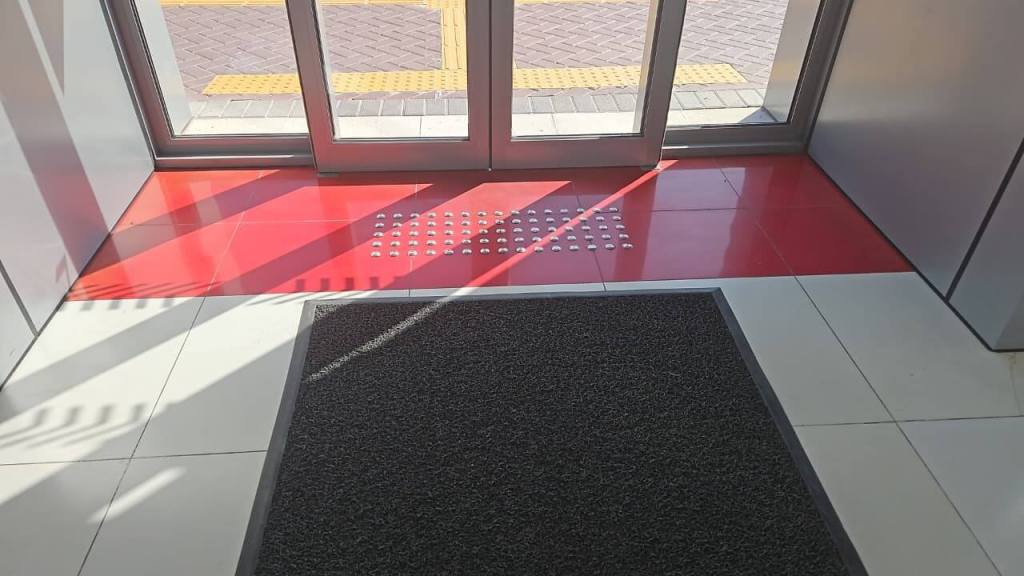 Interior entrance view showing a red-tiled area and a welcome mat near glass doors.