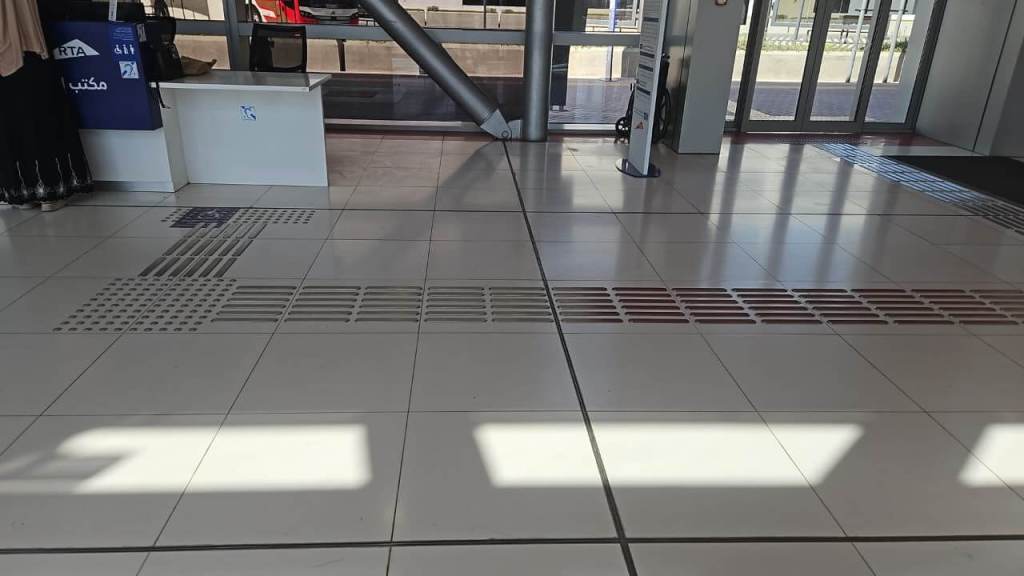 Interior view of a transport station showing tiled flooring with tactile paving, seating areas, and a service desk.